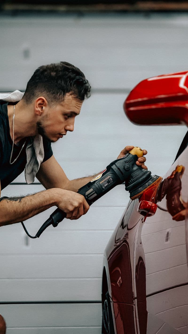 A detailer leaning in to polish the wing of a red car